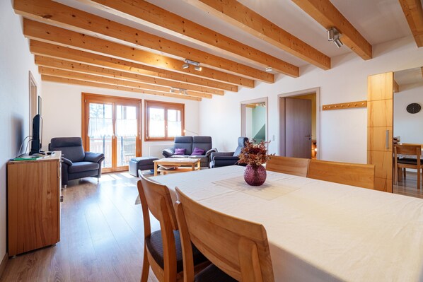 Un vaste espace de vie doté d’un plafond en bois, d’une table à manger avec des chaises, d’un canapé et d’un téléviseur posé sur un meuble.