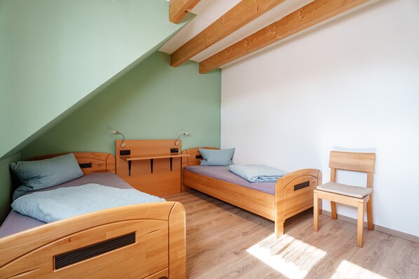 Una habitación con dos camas de madera, una silla de madera y un techo inclinado.