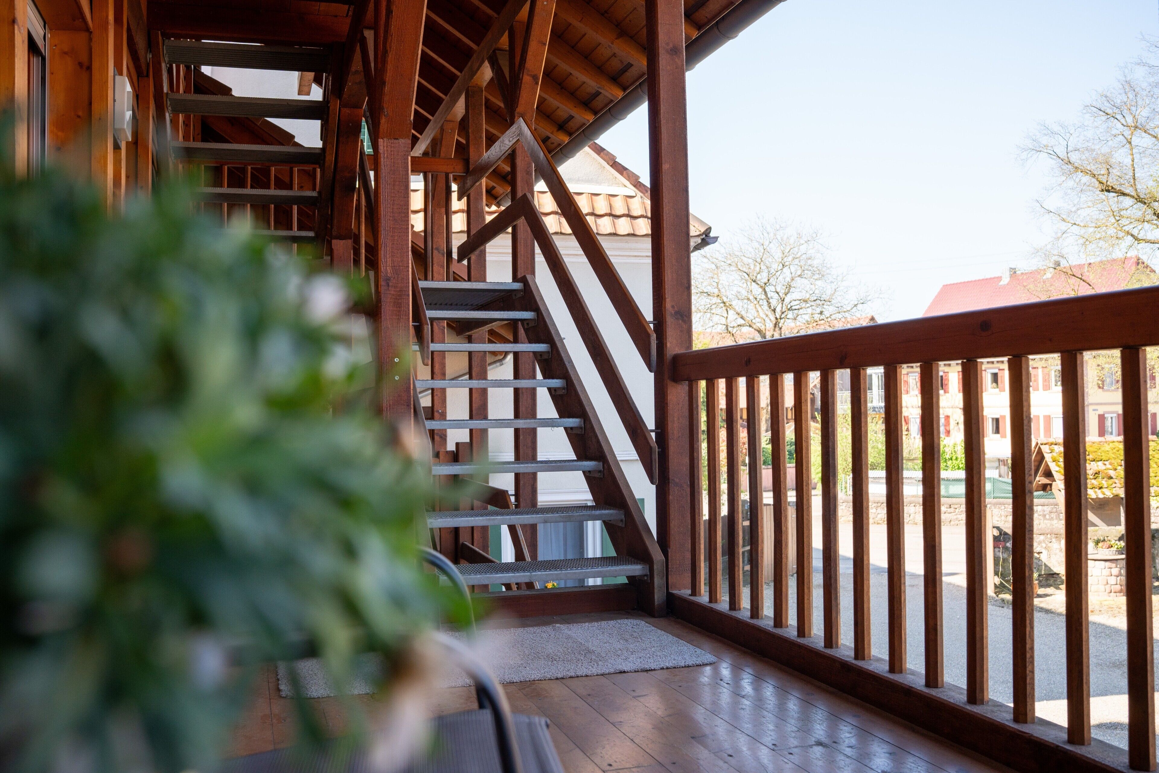 A wooden staircase leading to an upper level, a balcony with a railing, and a view of a residential area.