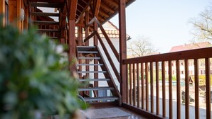 Una escalera de madera que conduce a un nivel superior, un balcón con barandilla y vista a una zona residencial.