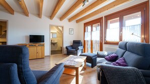 Una sala de estar moderna con vigas de madera, un televisor, un sofá, una silla y una mesa de comedor.