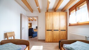 Una habitación con dos camas de madera, un armario, una ventana con cortinas y una puerta que da a otra habitación.