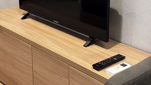 Una televisione a schermo piatto su un mobile porta TV in legno, con un telecomando e un piccolo dispositivo accanto.