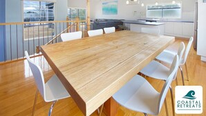 Un comedor amplio con una mesa de madera y sillas blancas, una cocina con armarios blancos, y un balcón con barandilla.