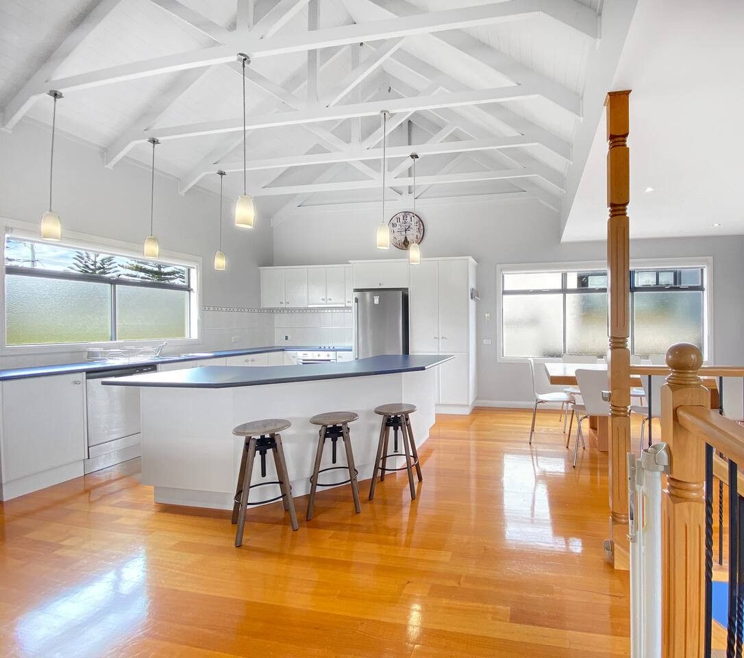 A spacious kitchen with a large island, wooden stools, and pendant lighting.