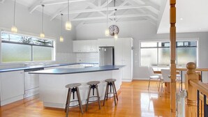 Une cuisine spacieuse avec un grand îlot central, des tabourets en bois et des luminaires suspendus.
