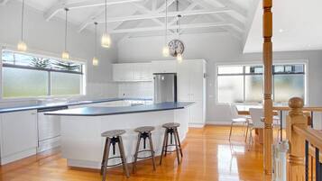 A spacious kitchen with a large island, wooden stools, and pendant lighting.