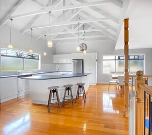 Une cuisine spacieuse avec un grand îlot central, des tabourets en bois et des luminaires suspendus.