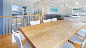 A spacious dining area with a wooden table and white chairs, a kitchen with white cabinets, and a balcony with a railing.