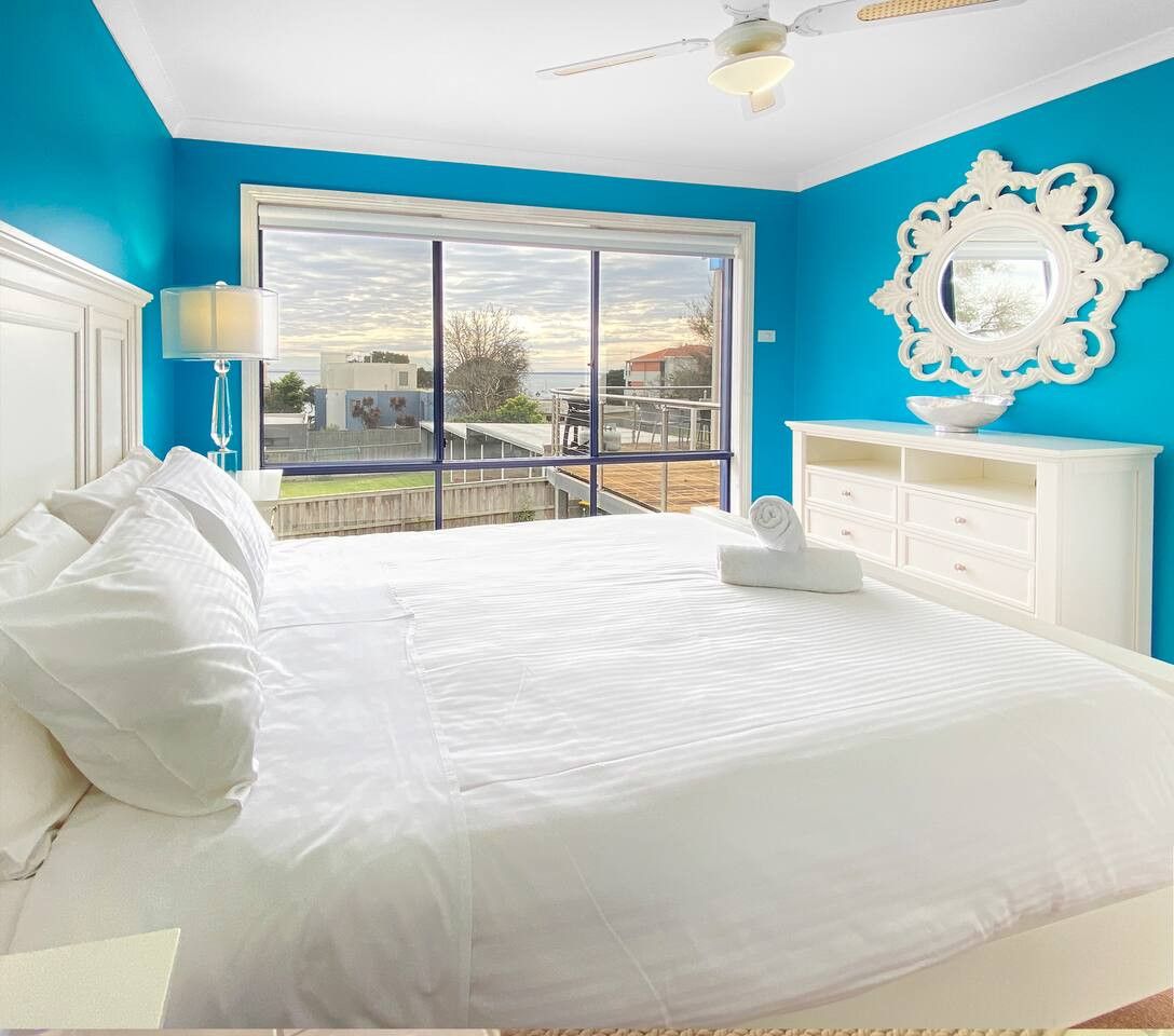 A bedroom with a large bed, a white dresser, a ceiling fan, and a view of the outdoors through a sliding glass door.