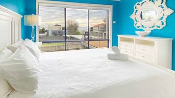 A bedroom with a large bed, a white dresser, a ceiling fan, and a view of the outdoors through a sliding glass door.