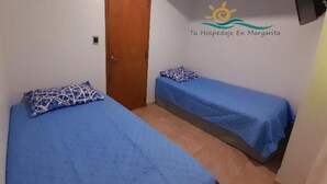 A small, simple room with two beds, a door, and a wall-mounted TV.