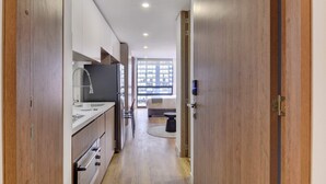 A narrow hallway with a kitchen area on the left, a window with a view of buildings on the right, and a door with a lock on the far end. - w Cozy Loft in the Heart of Bogot (Bogotá)
