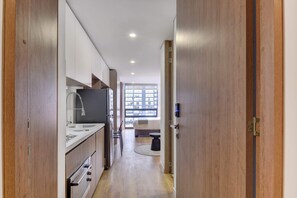 A narrow hallway with a kitchen area on the left, a window with a view of buildings on the right, and a door with a lock on the far end. - w Cozy Loft in the Heart of Bogot (Bogotá)