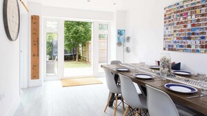 A dining area with a wooden table set for four, white chairs, a large wall clock, a family rule measuring tape, and a colorful wall art piece. - Modern Family Retreat Nr Beaches and Marina (Chichester)