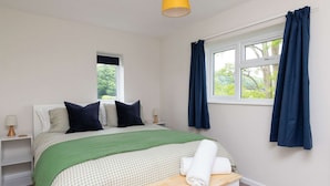 Quarto bem arrumado com cama, mesas de cabeceira, um banco e janela com cortinas.