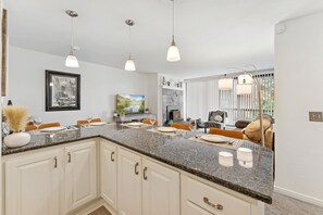 A kitchen with granite countertops, white cabinetry, pendant lighting, and a dining area with orange chairs. - Powder Pad Park Ave | Ski, Après & Downtown Fun (Park City)