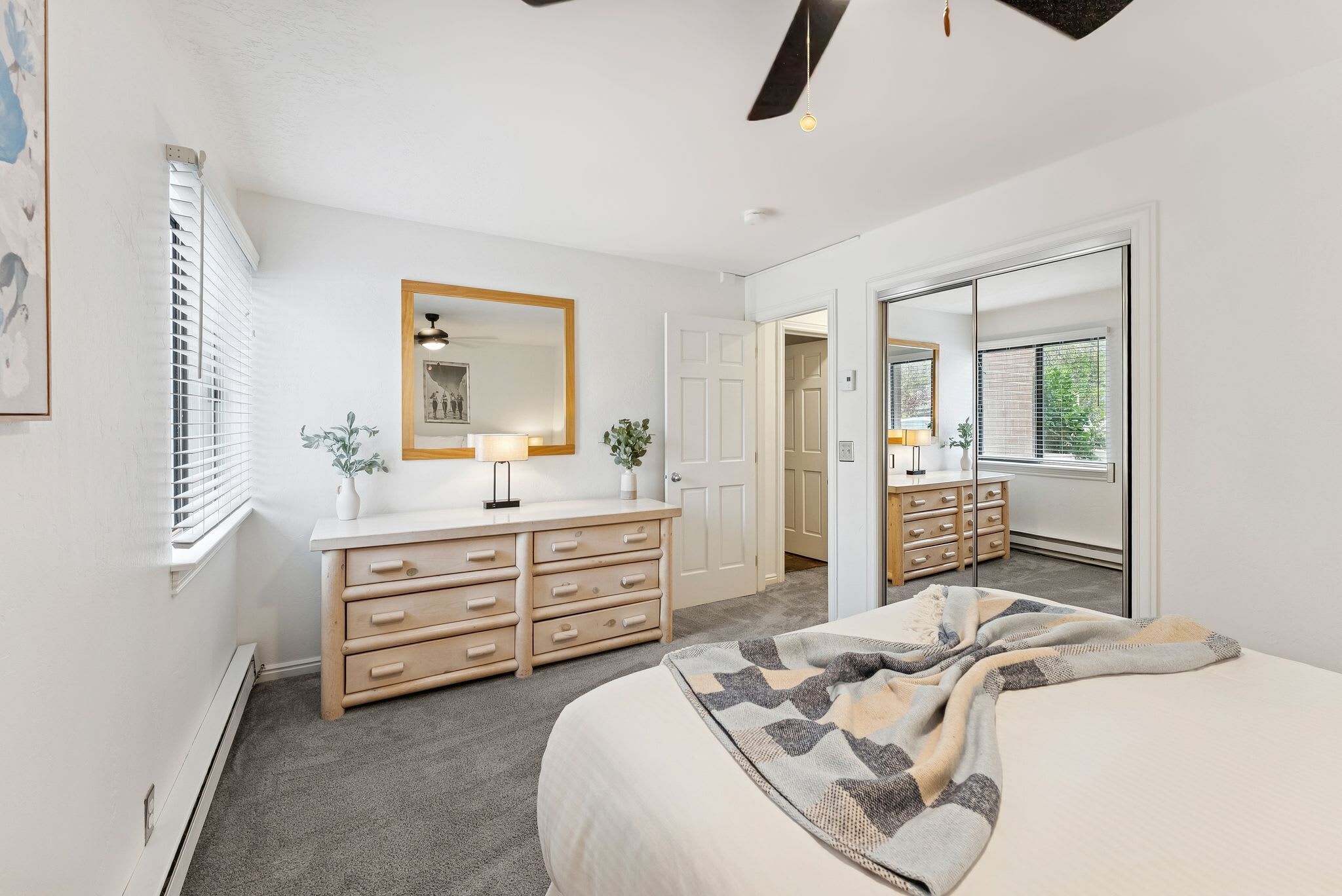A bedroom with a bed, a dresser, a mirror, and a door leading to another room.