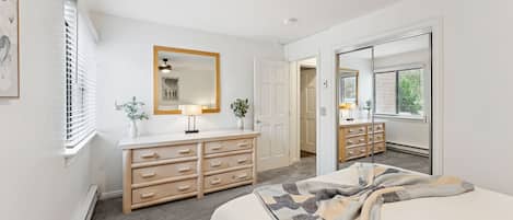 Un dormitorio con cama, cómoda, espejo y puerta que da a otra habitación.