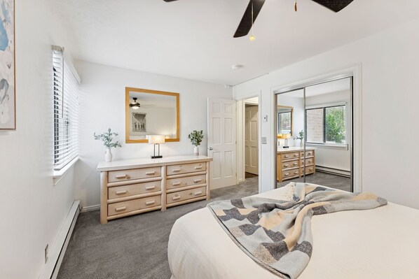 A bedroom with a bed, a dresser, a mirror, and a door leading to another room.
