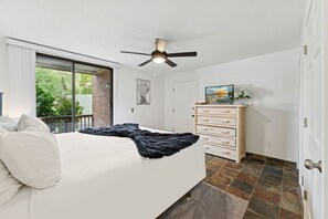 A bedroom with a bed, a ceiling fan, a dresser, and a window with a view of greenery. - Powder Pad Park Ave | Ski, Après & Downtown Fun (Park City)