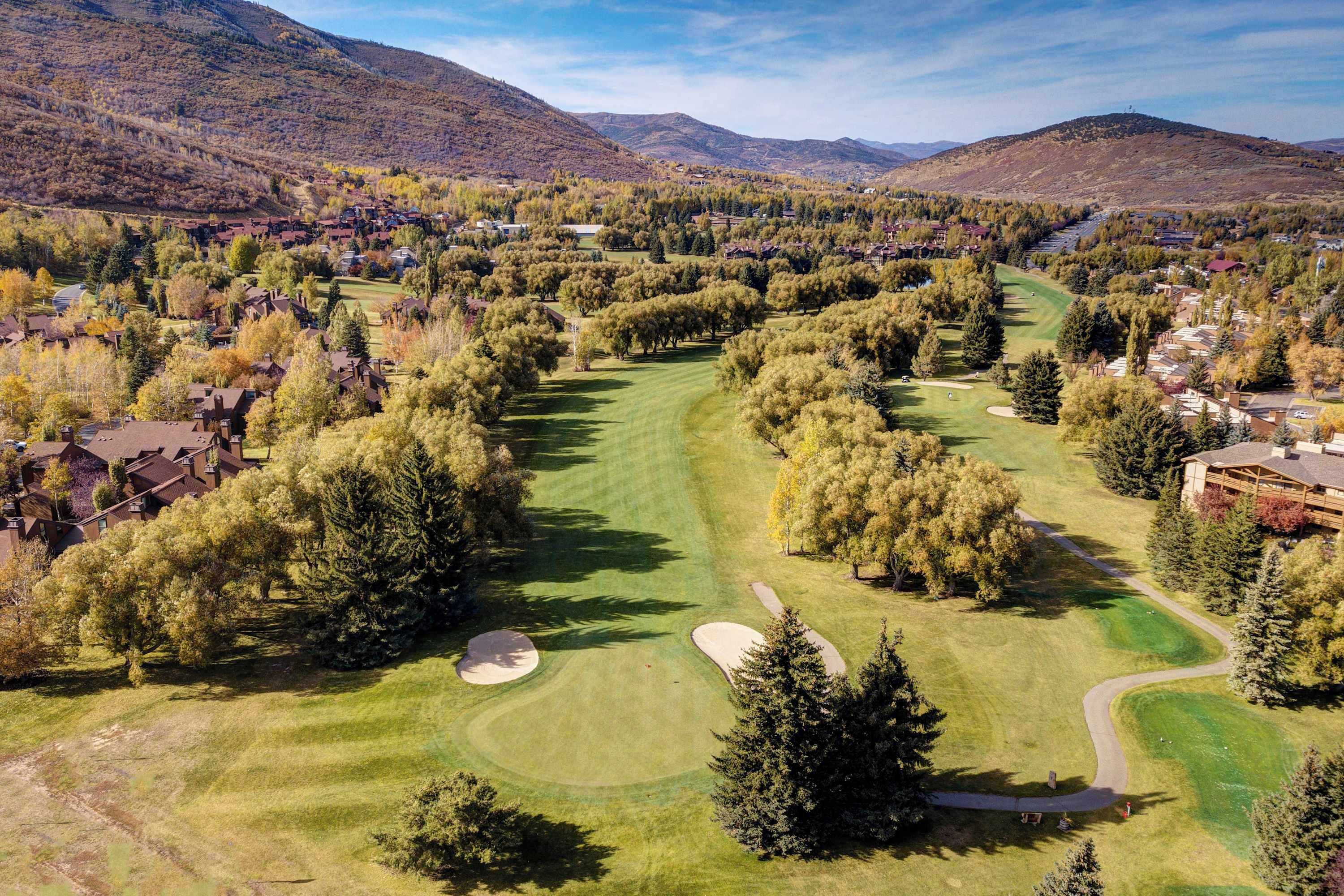 A golf course with a winding path, surrounded by trees and residential buildings.