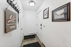 A narrow hallway with a door on the left, a coat rack above it, and a framed picture on the right. - Powder Pad Park Ave | Ski, Après & Downtown Fun (Park City)