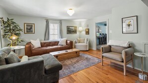 Una sala de estar con un sofá de cuero marrón, un sillón gris, una mesa de centro de madera y una mesita redonda con una lámpara.