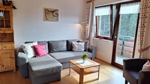 A living room with a grey sofa, a wooden coffee table, a wooden cabinet, and a painting on the wall. - Christianshof - Holiday Apartment '3' with Mountain View, Shared Garden and Wi-Fi (Oppenau)