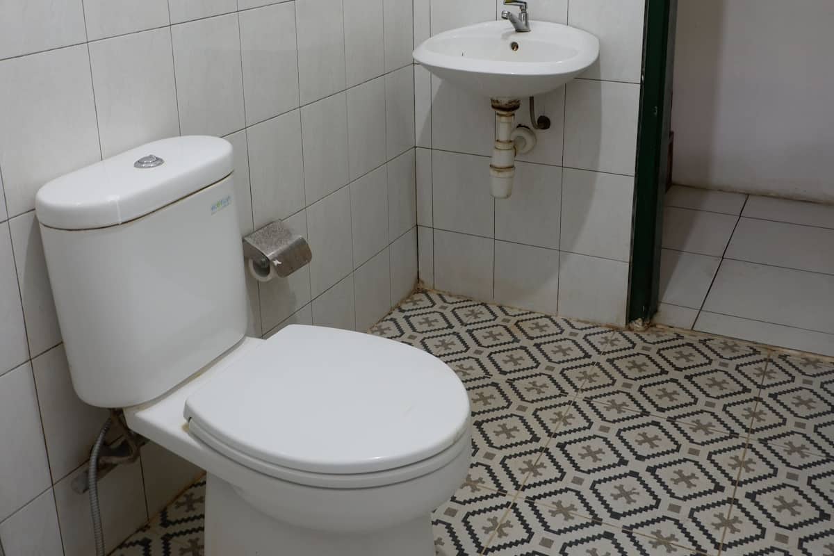 Casa de banho com sanita, lavatório e ladrilhos no chão com padrão.