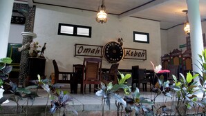 Interior de una cafetería con muebles de madera, un reloj de pared y plantas en macetas.