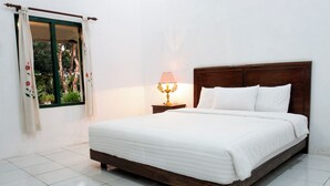 Una cama bien tendida con ropa blanca, un cabecero de madera y una mesita de noche con una lámpara.