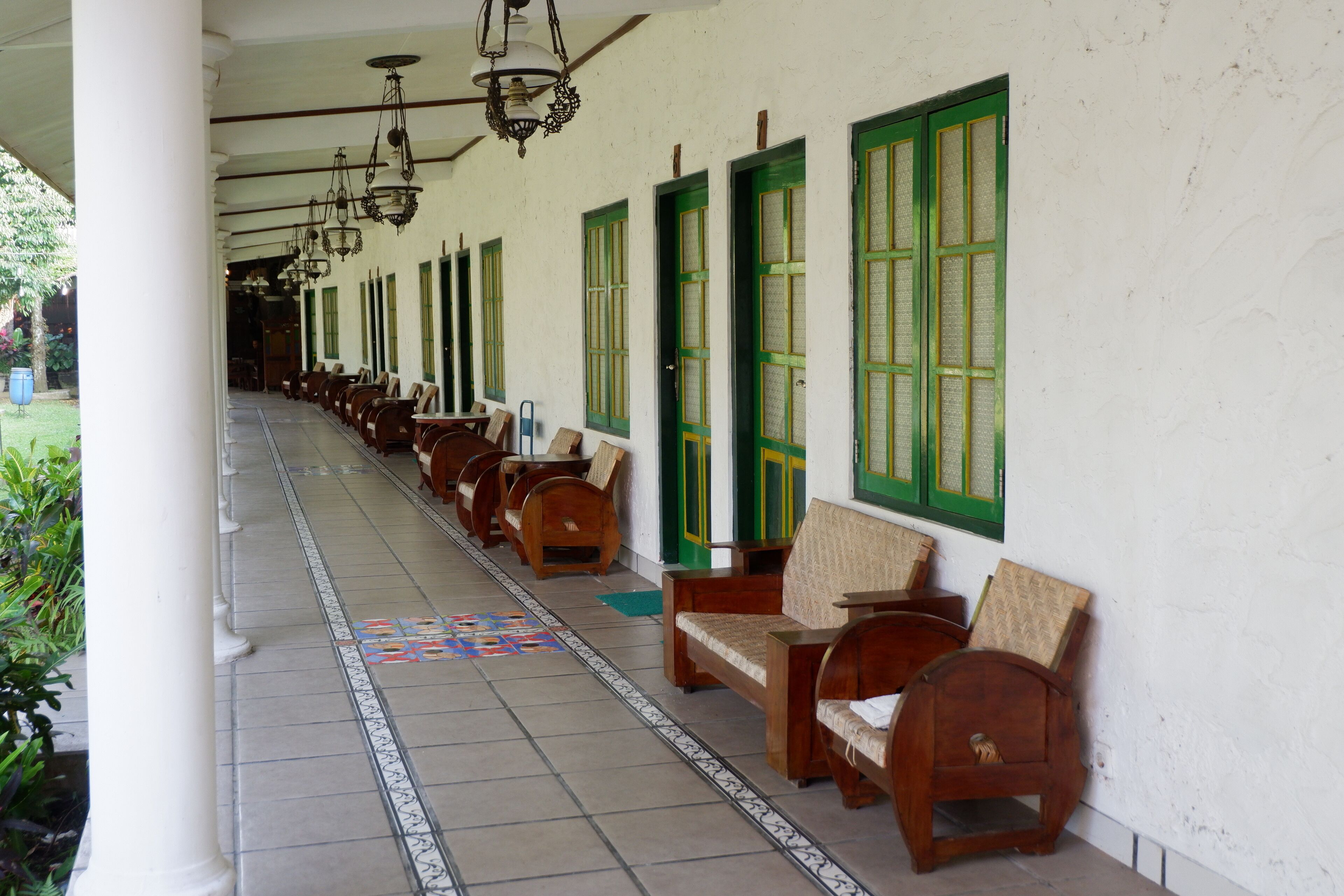 A covered corridor with rows of wooden benches and green-framed windows.