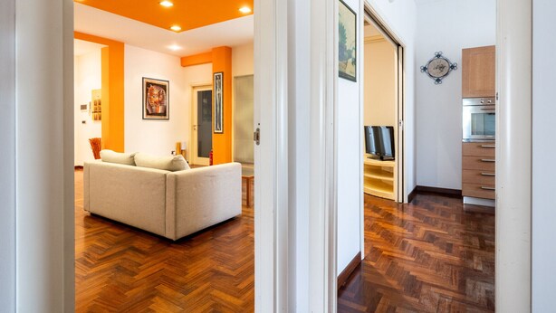 A modern living room with a sofa, a fireplace, and a kitchen area with wooden cabinets and a microwave. - Roomy Family Apartment by Wonderful Italy (Bari)
