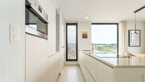 Una cocina moderna con armarios blancos, horno empotrado y un amplio ventanal con vistas a zonas verdes.