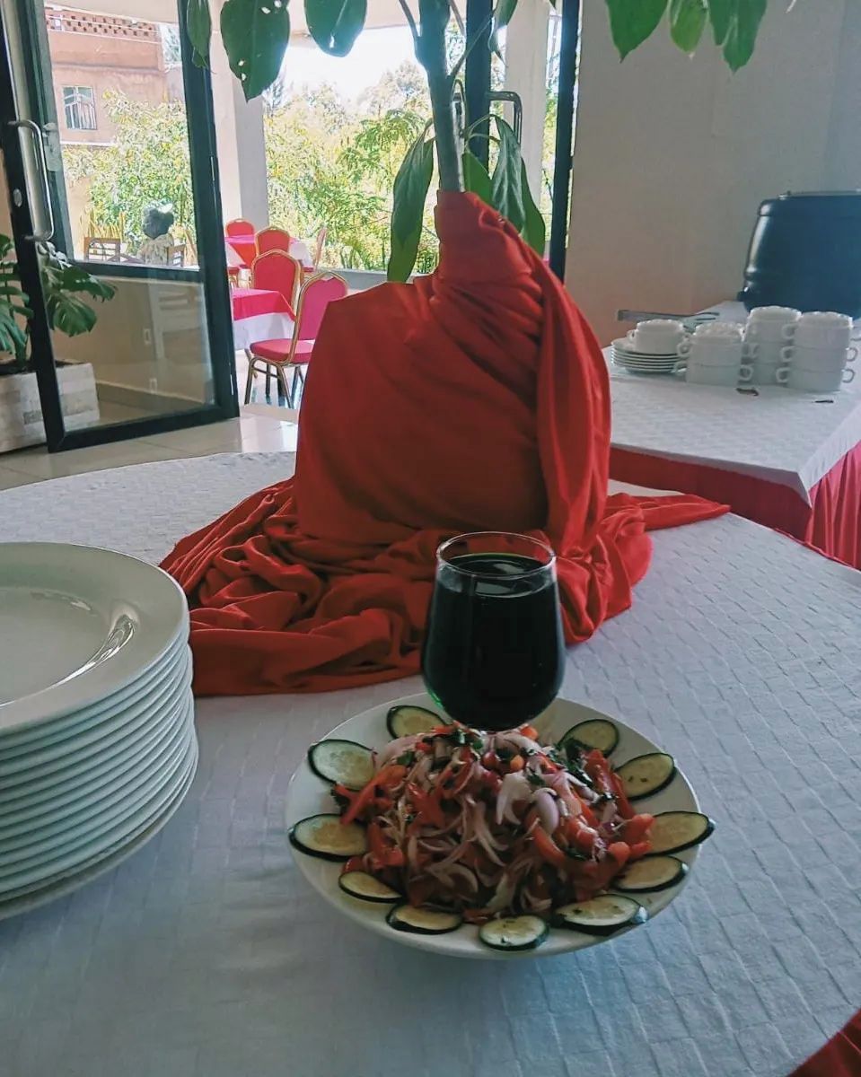 Una taula de dinar amb un plat de amanida i un got de vi negre, tot envoltat de cadires vermelles i una manta vermella.