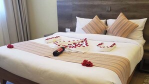 Un lit parfaitement fait, recouvert d’une couvre-lit à rayures, une bouteille de champagne et des pétales de roses rouges disposés dessus.