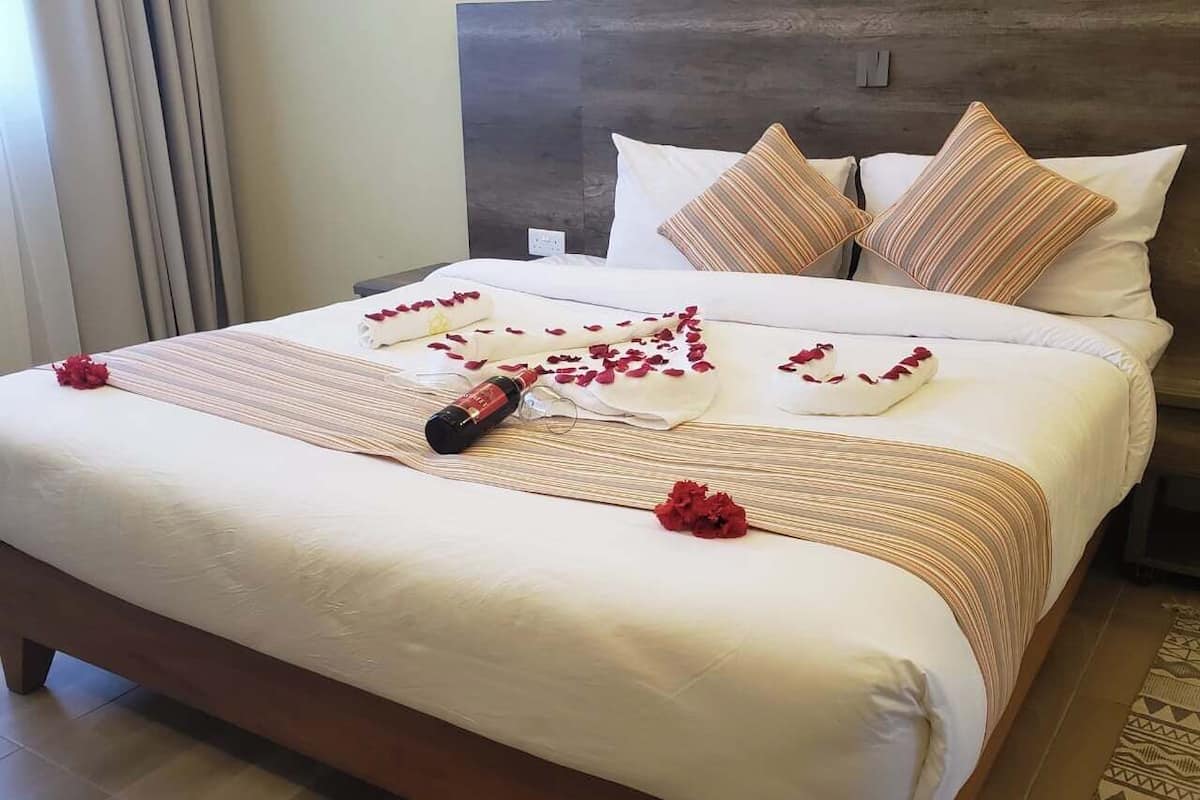 Una cama bien hecha con una colcha a rayas, una botella de champán y pétalos de rosa roja decorando la superficie.