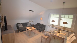 A modern living room with a sofa, armchair, coffee table, and a dining table with chairs. - Attic Apartment (Olsberg)