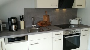 A modern kitchen with a dishwasher, coffee maker, toaster, and oven. - Attic Apartment (Olsberg)