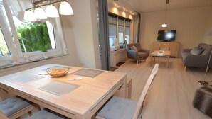 A modern living room with a wooden dining table, cushioned chairs, a sofa, and a TV. - Apartment with 2 Bedrooms, Sleeps up to 4 Guests (Olsberg)