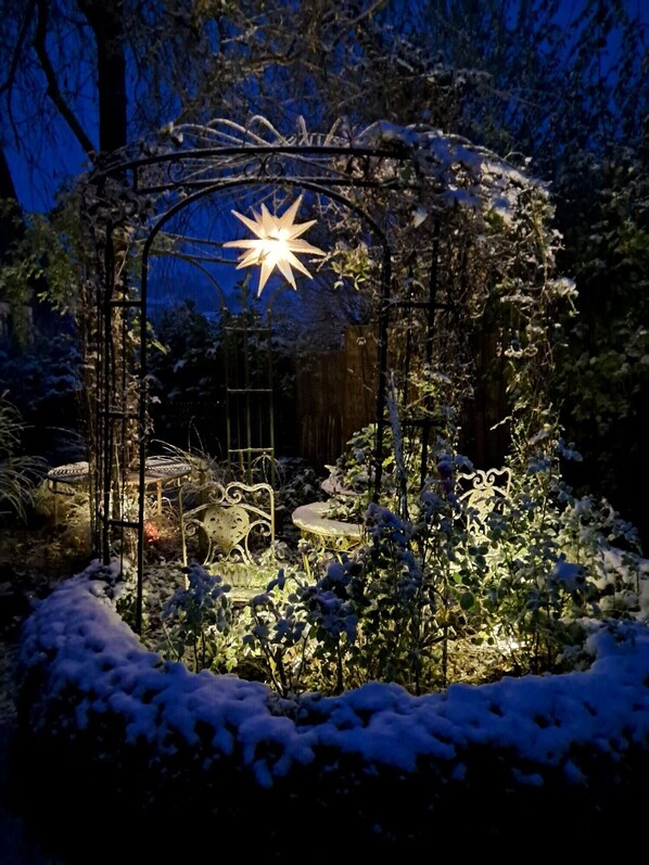 A snow-covered garden with a star-shaped light fixture at the center, surrounded by metal structures and plants.