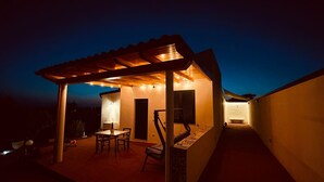 A covered patio area with a table and chairs, a bench, and string lights. - Il poggio (Agrigento)