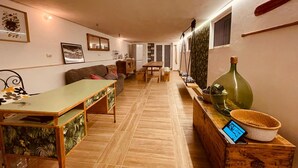A cozy living room with a sofa, a dining table, and a kitchen area with a wooden cabinet and a green bottle. - Il poggio (Agrigento)