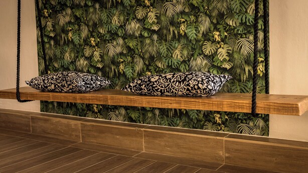 A wooden bench with two patterned cushions against a wall with a tropical leaf pattern. - Il poggio (Agrigento)