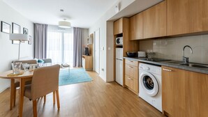 A modern kitchen with wooden cabinets, a built-in washing machine, and a dining area with a table and chairs. - Zenao Appart'hôtels Mâcon (Mâcon)