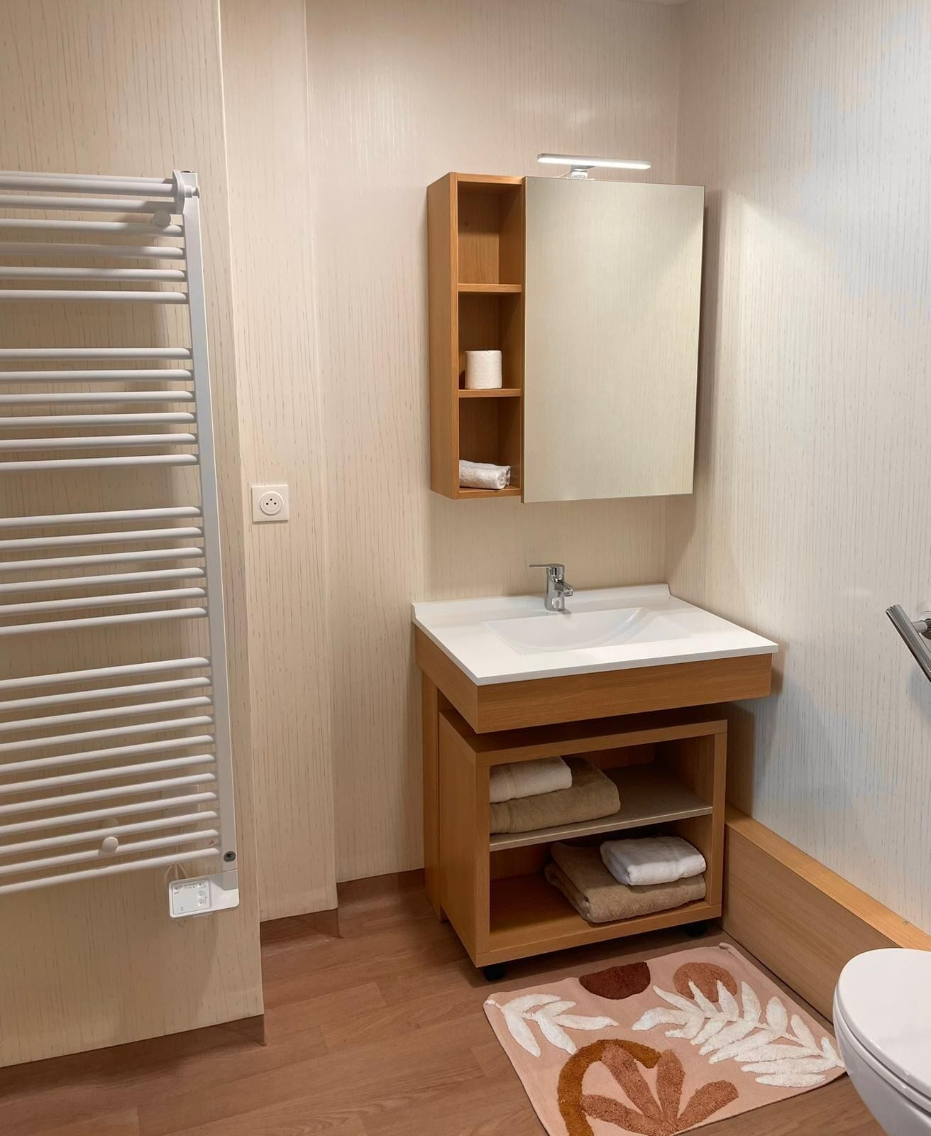 A compact bathroom with a white sink, wooden vanity, and a towel rack.