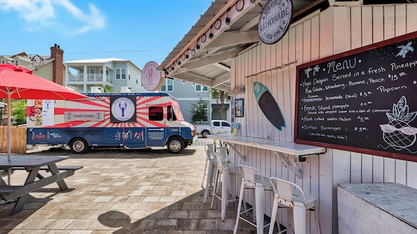 A food truck with a menu board, outdoor seating, and a clear sky.
