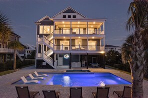 Une maison à deux étages située en bord de mer, dotée d’une piscine et d’un espace extérieur aménagé pour se détendre.