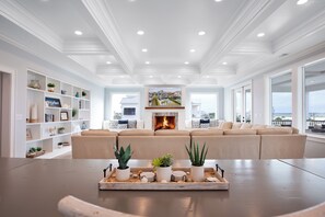 A spacious living room with a large beige sectional sofa, a fireplace, and a view of the ocean.